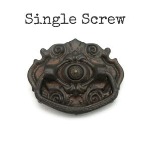 May include: Ornate, antique-style drawer pull with a dark bronze finish. The pull features a decorative oval center with a floral design and a curved handle. The text "Single Screw" is above the pull.