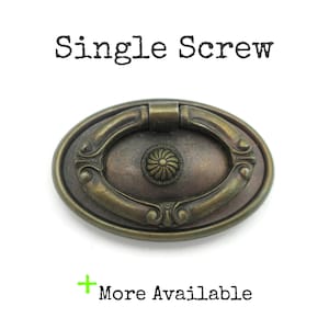 May include: An antique-style brass drawer pull with an oval shape and a decorative floral center. The pull has a ring handle and is mounted on a backplate. The text "Single Screw" is above the pull, and "More Available" is below.