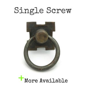 May include: A vintage bronze-toned drawer pull with a ring handle. The square backplate has a textured pattern. The text "Single Screw" is above the pull, and "More Available" is below. This hardware is suitable for cabinets and drawers.