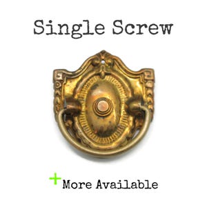 May include: Antique brass drawer pull with a decorative oval center and a curved handle. The text "Single Screw" is above the pull, and "More Available" is below it.