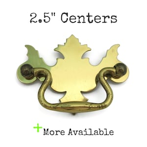 May include: A brass-coloured drawer pull with a decorative leaf design and a curved handle. The pull has a 6.35 cm centre-to-centre measurement. The text "2.5" Centers" is above the pull, and "More Available" is below.