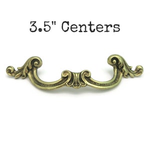 May include: Ornate brass-toned drawer pull with a curved design and decorative scrollwork. The text "3.5" Centers" is above the pull. This hardware is ideal for adding a vintage touch to furniture.