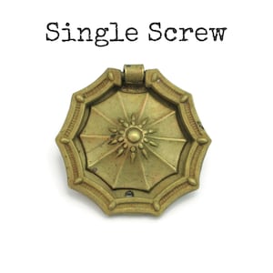 May include: A vintage brass-toned drawer pull with an octagonal shape and a sunburst design in the center. The text "Single Screw" is printed above the pull in black.