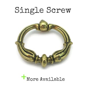 May include: An antique brass-toned drawer pull with a ring handle and decorative floral accents. The words "Single Screw" are printed above the pull, and "More Available" is printed below. The hardware is designed for furniture.