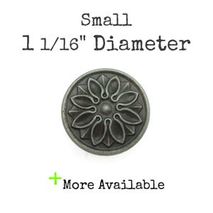 May include: A small, round, antique-style metal knob with a floral design. The knob is 1 1/16" in diameter and has a dark, weathered finish. Text on the image reads "Small 1 1/16" Diameter" and "More Available."