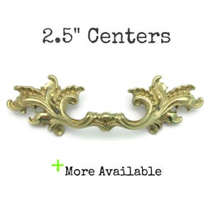 May include: Ornate brass drawer pull with a floral design. The pull measures 2.5 inches between the centers of the mounting holes. The text "2.5" Centers" and "More Available" are visible.
