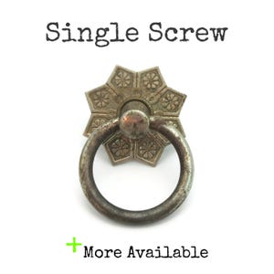 May include: A vintage-style metal drawer pull with a circular handle and a decorative, starburst-shaped backplate. The text "Single Screw" is above the pull, and "More Available" is below it.