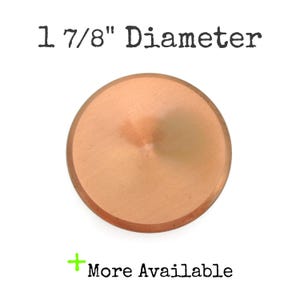 May include: A copper-colored, circular object with a diameter of 1 7/8 inches. The text "1 7/8" Diameter" is above the object, and "More Available" is below. The object has a slightly raised center and a smooth surface.