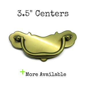 May include: A brass-colored metal drawer pull with a curved, swinging handle and a decorative backplate. The text 3.5" Centers is printed above the hardware, and the text + More Available is printed below the hardware on a white background.