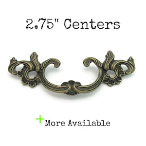 May include: Antique brass-colored drawer pull with ornate floral design. The pull measures 2.75 inches between the centers of the mounting holes. The text "2.75" Centers" and "More Available" are visible.