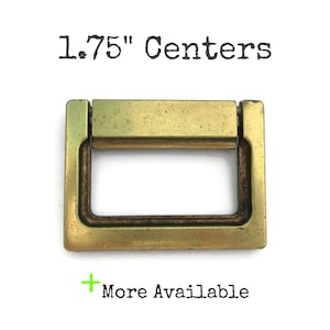 May include: A brass cabinet pull with a 1.75" center to center measurement. The pull has a rectangular shape with a recessed center.