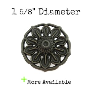 May include: Bronze-colored floral cabinet knob with a diameter of 1 5/8 inches. The knob features a detailed, openwork design with a central circular element and petal-like shapes. Text reads "1 5/8" Diameter" and "More Available".