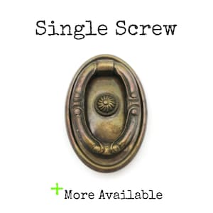 May include: An antique brass-toned oval drawer pull with a decorative handle and a central floral design. The text "Single Screw" is above the pull, and "More Available" is below.