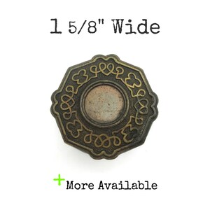 May include: An octagonal bronze-toned metal button measuring 1 5/8" wide. The button features a central circular recessed area surrounded by a decorative border of raised, interconnected scrollwork and clover-like shapes. Text reads 1 5/8" Wide and More Available.