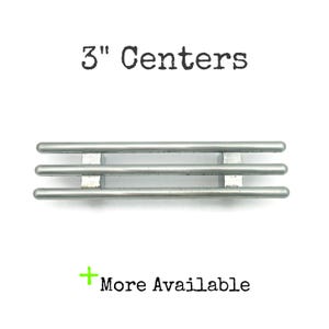 May include: A silver-colored cabinet pull with three horizontal bars, 3 inches (7.6 cm) apart, and a rectangular mounting bracket. The text "3" Centers" and "More Available" are also visible.