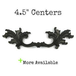 May include: A dark-colored metal drawer pull with an ornate, scrolling leaf-like design. The text 4.5" Centers is printed above the handle, and the text + More Available is printed below the handle, indicating the hardware size and availability.
