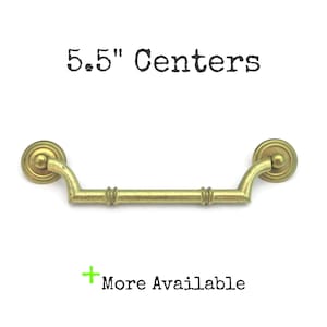 May include: A brass-colored drawer pull with a curved handle and circular end pieces. The text "5.5" Centers" is above the pull, and "More Available" is below it.