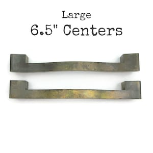 May include: Two antique-style metal drawer pulls with a distressed finish. The pulls are rectangular with a curved center and measure 6.5 inches between the centers. The word "Large" and "6.5" Centers" are printed above the pulls.