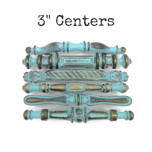 May include: Six drawer pulls with 3" Centers text above. Each pull features a distressed turquoise blue finish with dark bronze metallic accents. The hardware pieces display varied decorative shapes, including ribbed, twisted, and smooth profiles.