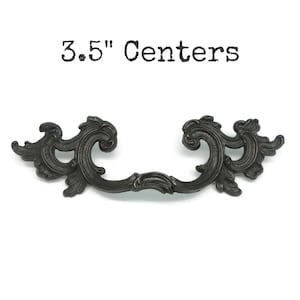 May include: A dark bronze-colored metal drawer pull with an ornate, scrolling leaf design and a curved handle. The text 3.5" Centers is printed above the hardware, indicating the distance between the two mounting points for installation.