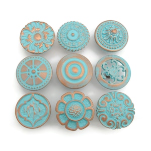 May include: Nine decorative cabinet knobs in various designs. Each knob features a turquoise finish with bronze accents. The knobs have different floral and geometric patterns, including a flower, a circle with concentric rings, and a circular openwork design.