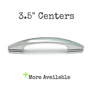 May include: A polished silver-toned metal cabinet pull with a curved arch shape and three horizontal engraved lines on each end. The text 3.5" Centers is displayed above the handle, and the text + More Available is displayed below.