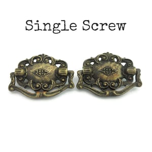 May include: Two antique brass drawer pulls with ornate detailing. Each pull features a decorative oval center with a handle and curved base. The text "Single Screw" is above the pulls.