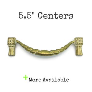 May include: A brass-toned cabinet pull with a rope-like center and decorative end pieces. The text "5.5" Centers" is above the pull, and "More Available" is below it.