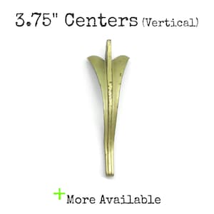 May include: A vertical brass-toned metal drawer pull with a flared top and a slender, tapering body. The text 3.75" Centers (Vertical) is printed above the object, and the text More Available is printed below with a green plus sign.