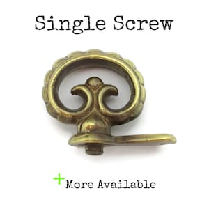 May include: A single brass screw with an ornate, scrolled design. The screw features a circular handle with a decorative edge and a small, rectangular base. The text "Single Screw" is above the screw, and "More Available" is below.