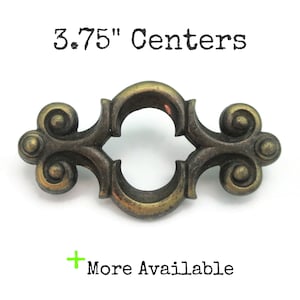 May include: Ornate bronze-toned cabinet pull with a decorative design. The pull has a central opening and scrollwork details on each end. The text "3.75" Centers" is above the pull, and "More Available" is below.