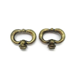 May include: Two identical antique brass drawer pulls featuring a rounded, oval-shaped handle design with a central mounting post at the base. The metal has a weathered, darkened patina finish with visible highlights on the curved edges.