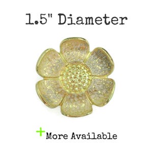 May include: A gold-colored metal flower with a textured surface. The flower has six petals and a center with a raised, textured design. The flower is 1.5 inches in diameter.