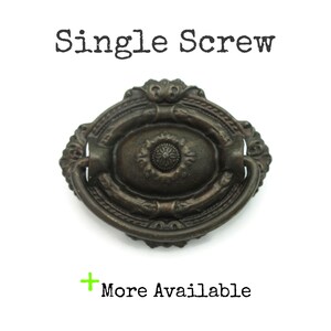 May include: An antique bronze-colored drawer pull with an oval center and a decorative floral design. The pull has a curved handle and is labeled "Single Screw" above and "More Available" below.
