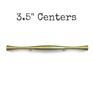 May include: A brass-toned cabinet pull with a curved, elongated design. The text "3.5" Centers" is above the pull. The pull measures 3.5 inches in length, suitable for drawers and cabinets.
