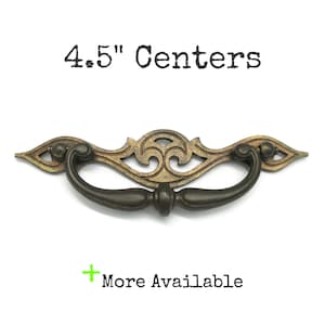 May include: An antique-style drawer pull with a dark bronze finish. The pull has a decorative filigree design and a curved handle. The text "4.5" Centers" and "More Available" are visible.
