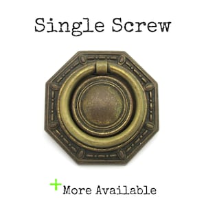 May include: An antique brass-toned octagonal drawer pull with a ring handle. The pull has an ornate design around the edges and a circular centre. The text "Single Screw" is above the pull, and "More Available" is below.
