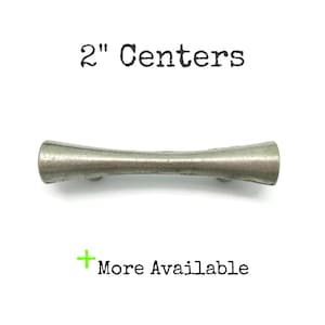 May include: A silver-toned cabinet pull with a curved, hourglass shape. The text "2" Centers" is above the pull, and "More Available" is below. The pull measures 2 inches in length.