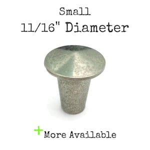 May include: A small, silver-toned cabinet knob with a rounded top and a cylindrical base. The knob has a diameter of 11/16 inches. The text "Small 11/16" Diameter" is above the knob, and "More Available" is below.