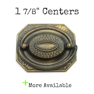 Peut inclure: Tirette de tiroir en laiton antique avec un centre ovale et des motifs floraux décoratifs. La tirette a une poignée et mesure 4,76 cm entre les centres. Le texte "More Available" est visible.
