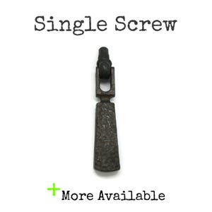 May include: A dark gray metal drop pull with a textured, hammered surface and a single screw attachment point. The text "Single Screw" appears at the top, and the text "+ More Available" is printed in green at the bottom of the image.