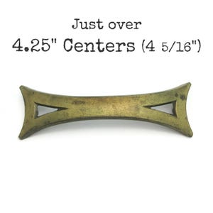 May include: A brass-coloured, decorative cabinet pull with a unique, arrow-shaped design. The pull measures just over 4.25 inches between the mounting holes, or 4 5/16 inches.