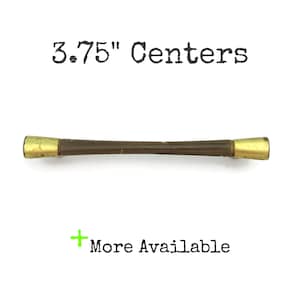 May include: A brown wooden cabinet pull with gold-toned metal ends. The pull measures 3.75 inches between the centers of the mounting holes.  "More Available" is written in green below the pull.