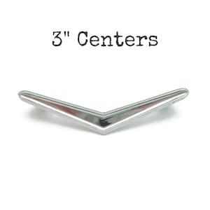 May include: A chrome-finished, V-shaped cabinet pull with a 3-inch center-to-center measurement. The hardware has a reflective surface and is set against a white background. The text "3" Centers" is above the pull.