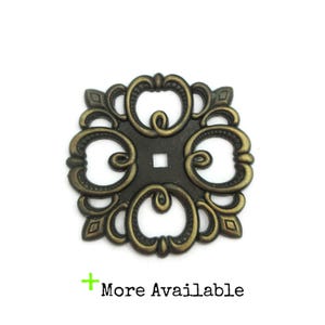May include: Ornate, square bronze-toned metal furniture hardware with a central square and decorative scrollwork. The words "More Available" are in the lower left corner.