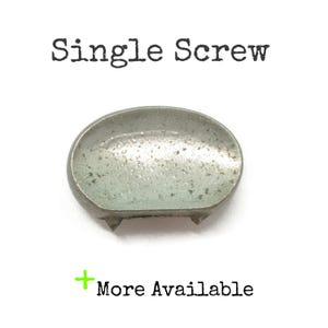 May include: A metallic, semi-circular stud with a speckled, light grey finish and two small prongs on the bottom edge. The text "Single Screw" appears above the object, and "+ More Available" is printed below the item on a white background.