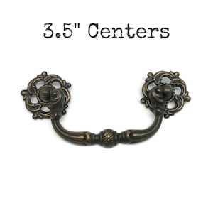 May include: A dark bronze-toned metal drawer pull with a curved handle and two circular, ornate backplates featuring scrollwork details. The text 3.5" Centers is printed above the hardware, indicating the distance between the mounting points.