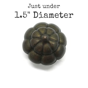May include: A dark bronze-toned metal knob with a rounded, multi-lobed floral shape. The object features a textured, aged finish and is labeled with the text Just under 1.5" Diameter, indicating its size for potential hardware applications.