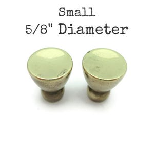 May include: Two small cabinet knobs with a light green, rounded top and a brass-colored base. The knobs are labeled "Small" and "5/8" Diameter".