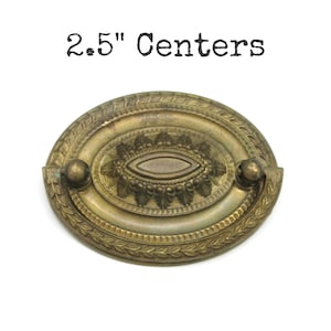 May include: Vintage brass oval drawer pull with a detailed floral design. The pull has a 6.35 cm centre-to-centre measurement and features two small ball-shaped handles. The text "2.5" Centers" is printed above the pull.